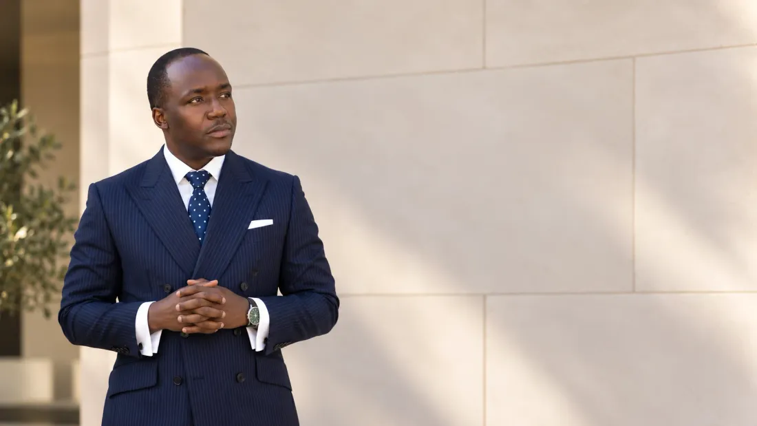 Dr. Job Mogire in a navy pinstripe suit, standing against a limestone wall